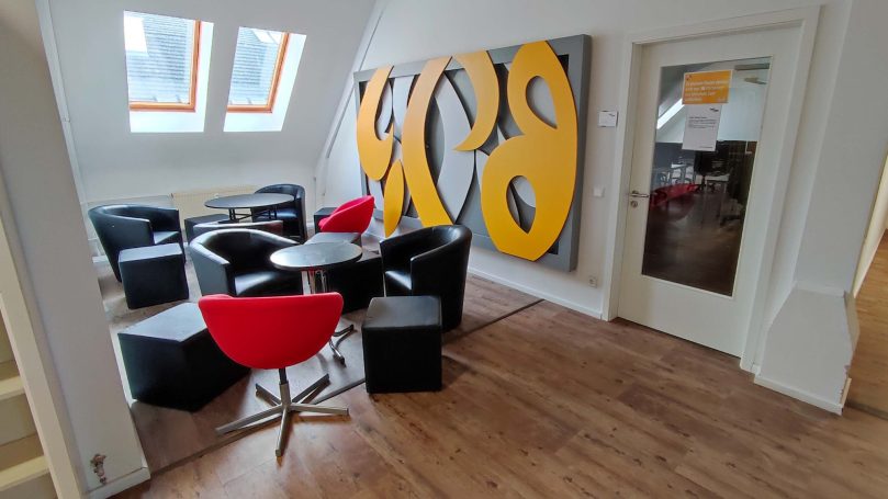 Moderne Sitzecke mit schwarzen und roten Stühlen sowie einem großen, orangefarbenen Kunstwerk.