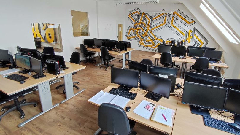 Büro mit mehreren Schreibtischen, Computern und einer bunten Wandgestaltung.